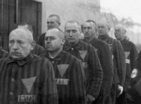 Prisoners wearing pink triangles on their uniforms are marched outdoors by Nazi guards at the Sachsenhausen. Photo credit: Auschwitz-Birkenau State Museum.