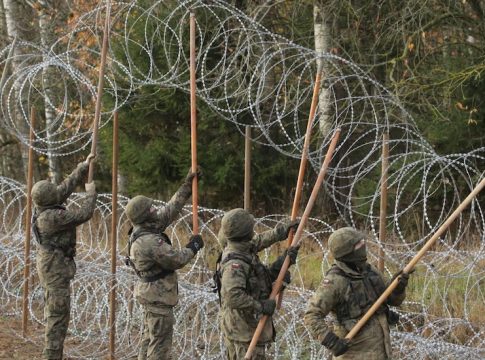 Polish troops lift coils of razor wire into place along the border.